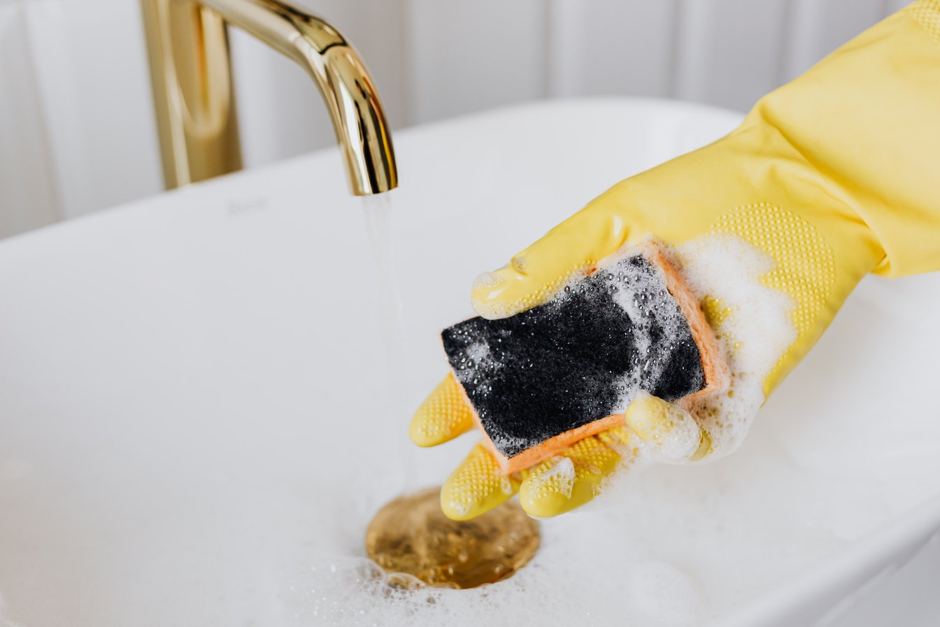 Person in glove using detergent and sponge while cleaning sink